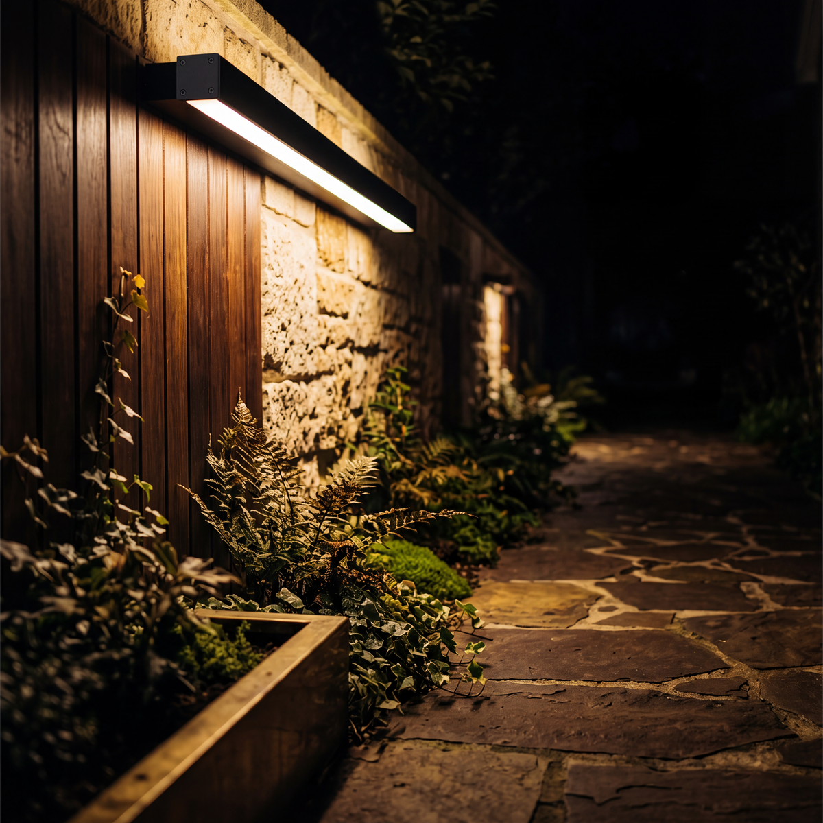Outdoor wall light lighting foliage and a stone path at night